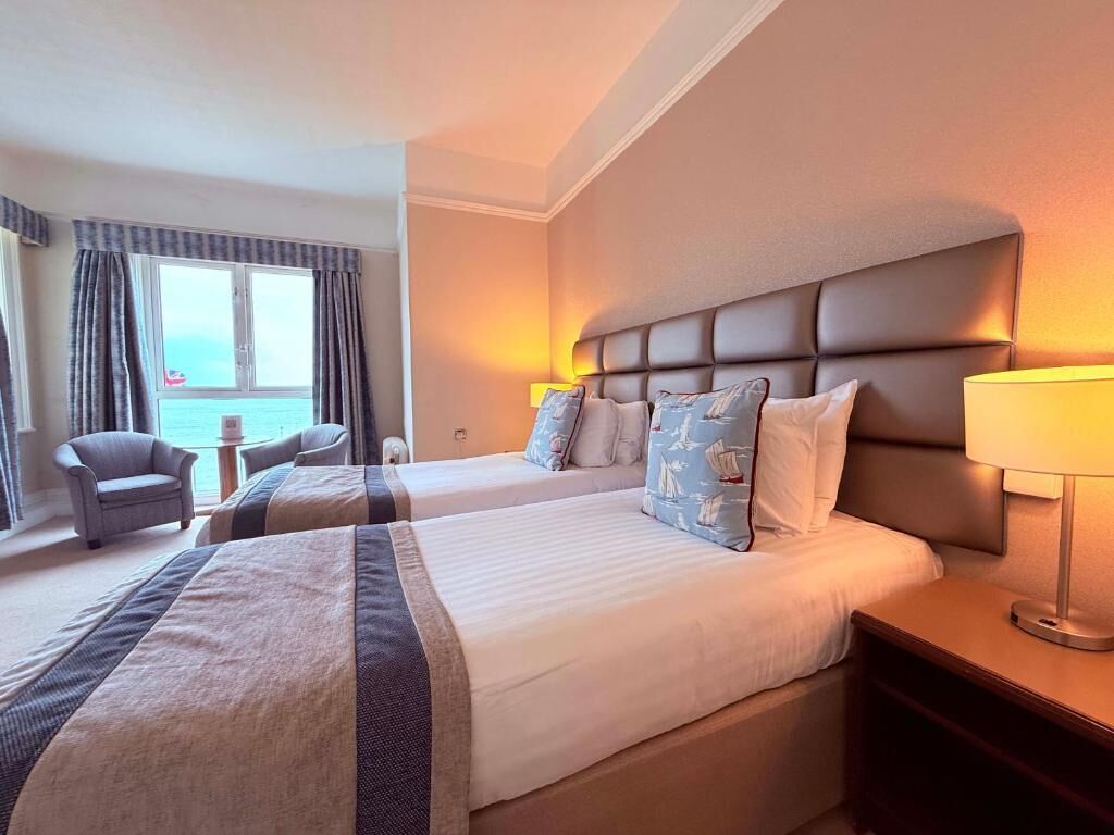 Een hotelkamer met twee bedden, een stoel, een lamp en uitzicht op zee.
