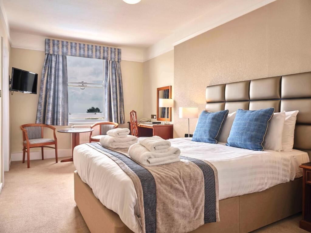A hotel room with a large bed, a desk, a chair, a TV, and a window with curtains.