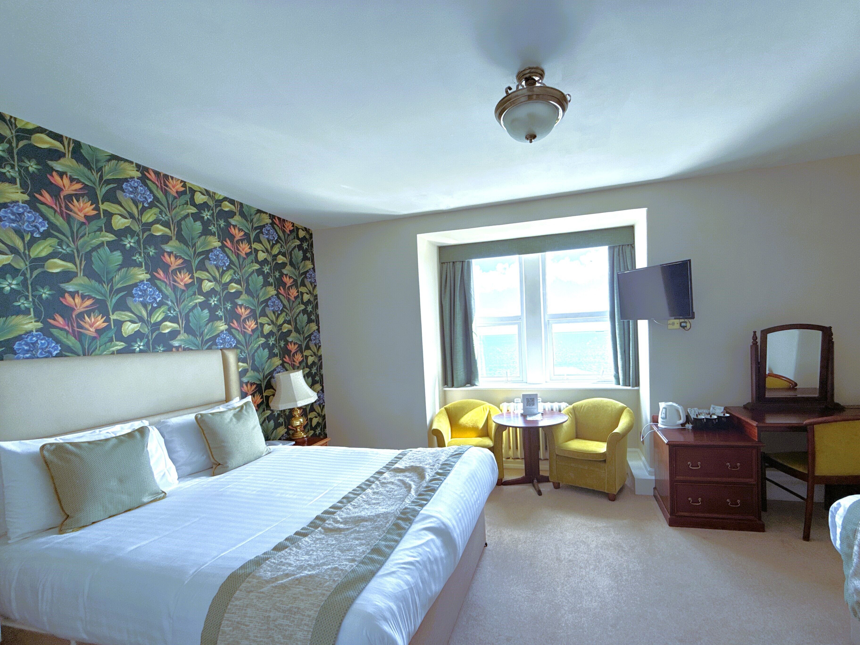 Habitación de hotel con una cama grande, dos sillas, una mesita, televisión y cómoda.