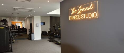 A fitness studio with exercise equipment, a digital display, and a neon sign on the wall.
