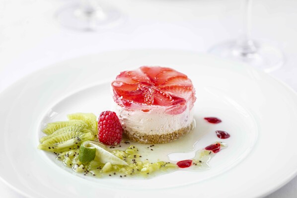 A dessert with a strawberry topping, kiwi slices, and a raspberry on a white plate.
