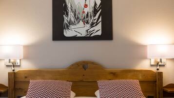 A hotel room with a wooden headboard, two patterned pillows, a wall-mounted picture of a snowy mountain scene, and bedside lamps.