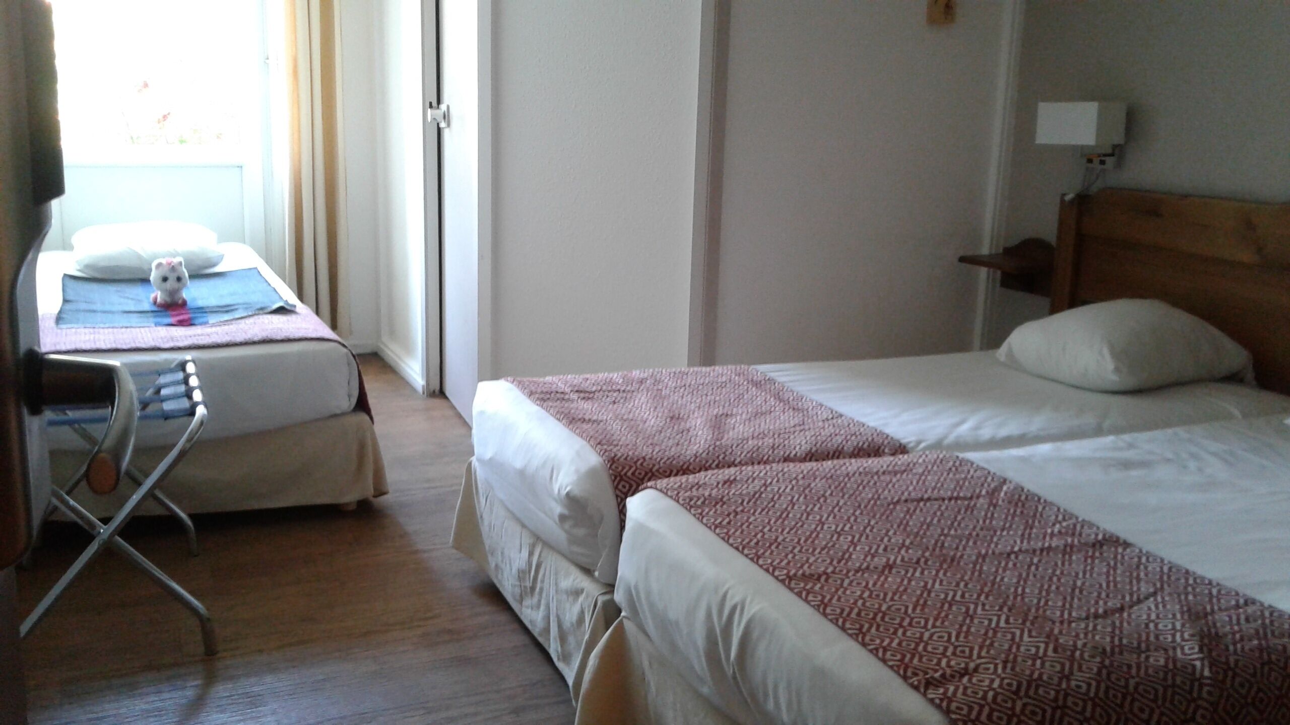 Een hotelkamer met twee bedden, een bureau met stoel en een raam met gordijnen.
