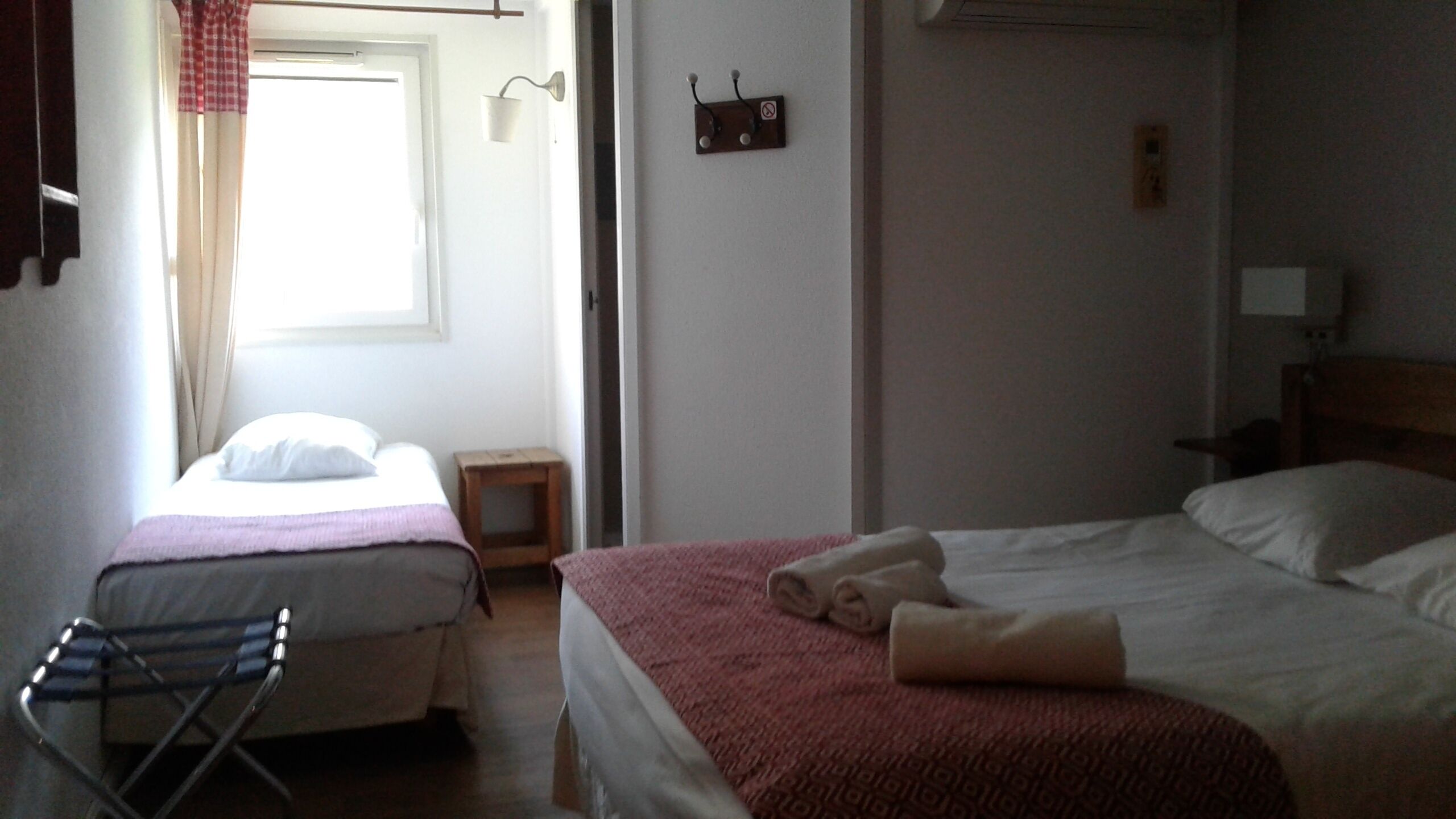 A hotel room with two beds, a small table, a chair, and a window with curtains.