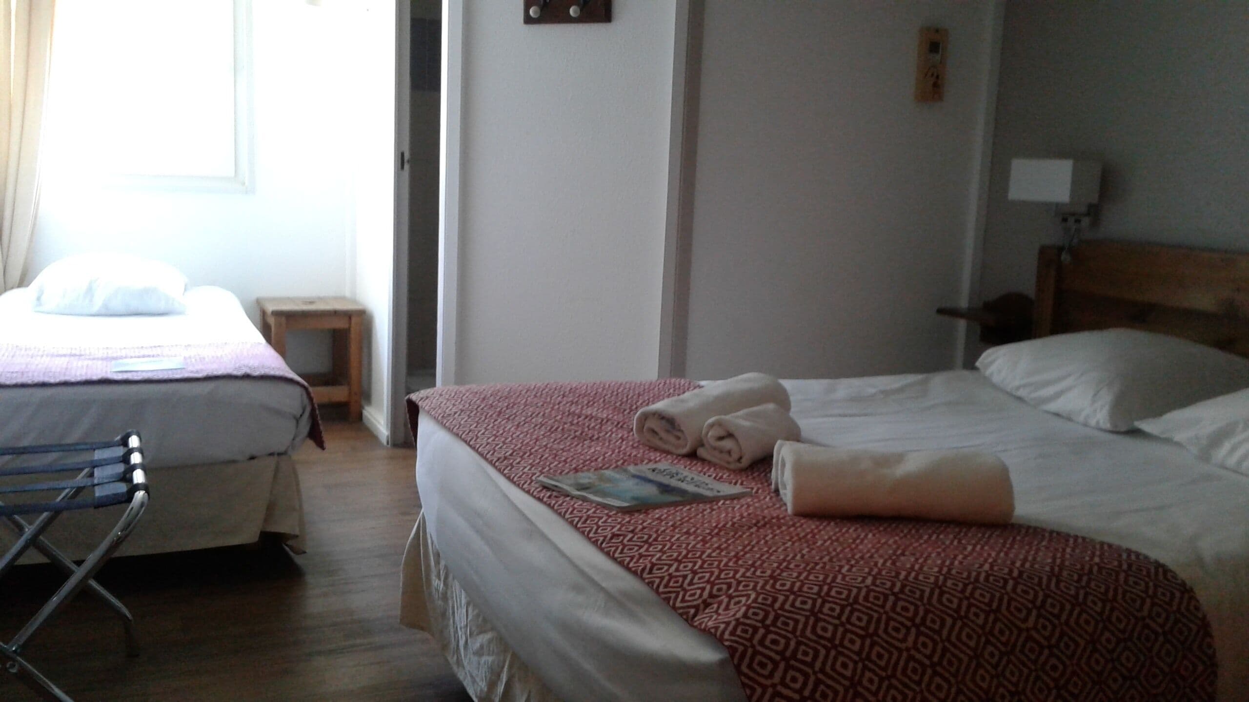 A hotel room with two beds, a small table, and a chair.