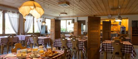Un espace repas avec des nappes à carreaux, des chaises en bois et des lampes suspendues.