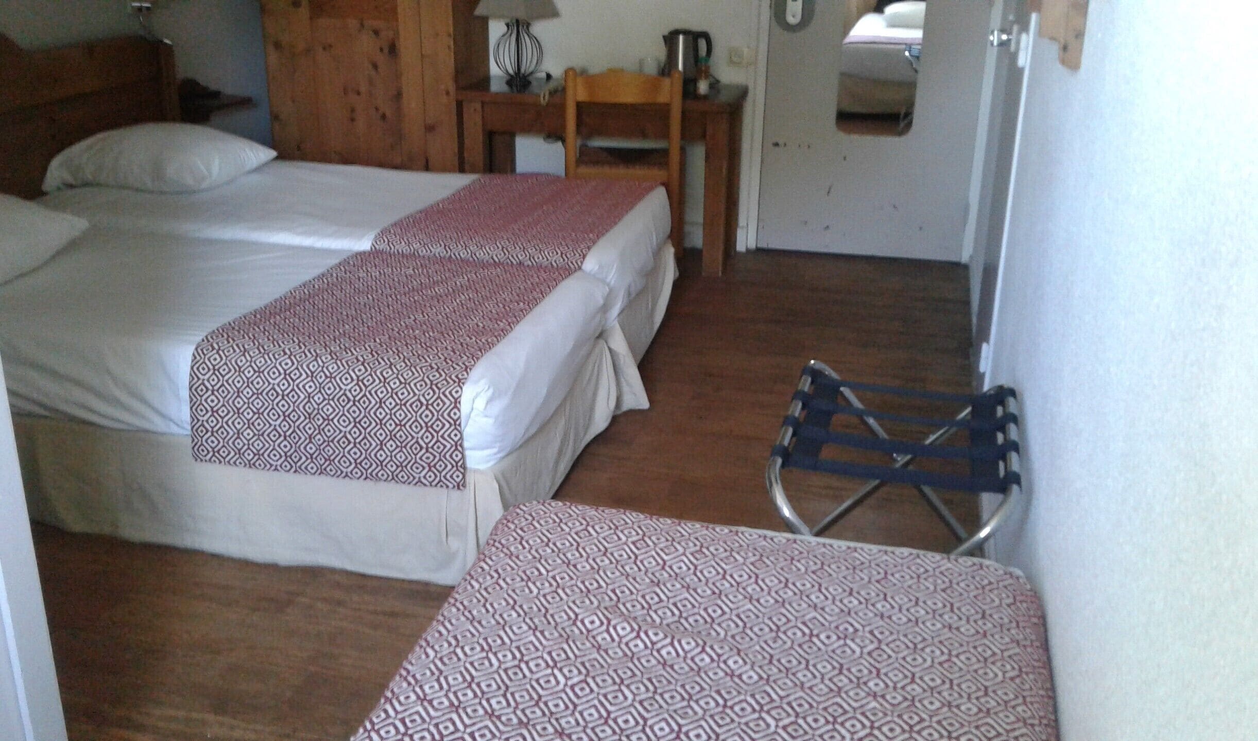 Una habitación con dos camas, cabecero de madera, una mesita con lámpara y una silla.