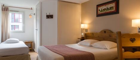 A room with two beds, a wooden headboard, a small table, a wall-mounted lamp, and a framed picture.