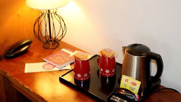 Une table en bois avec une lampe, un téléphone, un carnet, deux tasses rouges, des sachets de thé Lipton, une machine à café et un plateau.