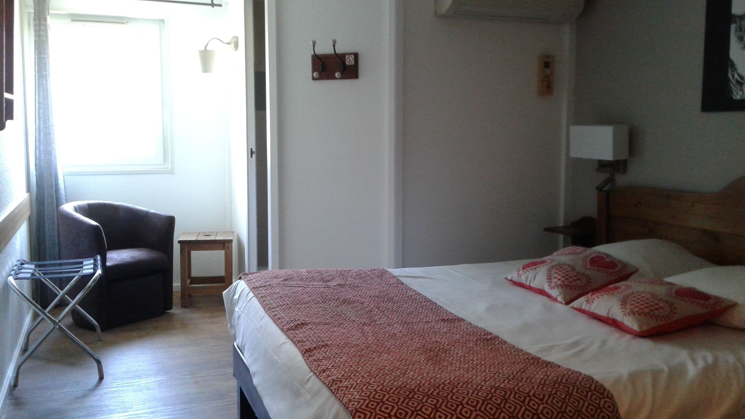 A hotel room with a bed, a chair, a small table, and a window.