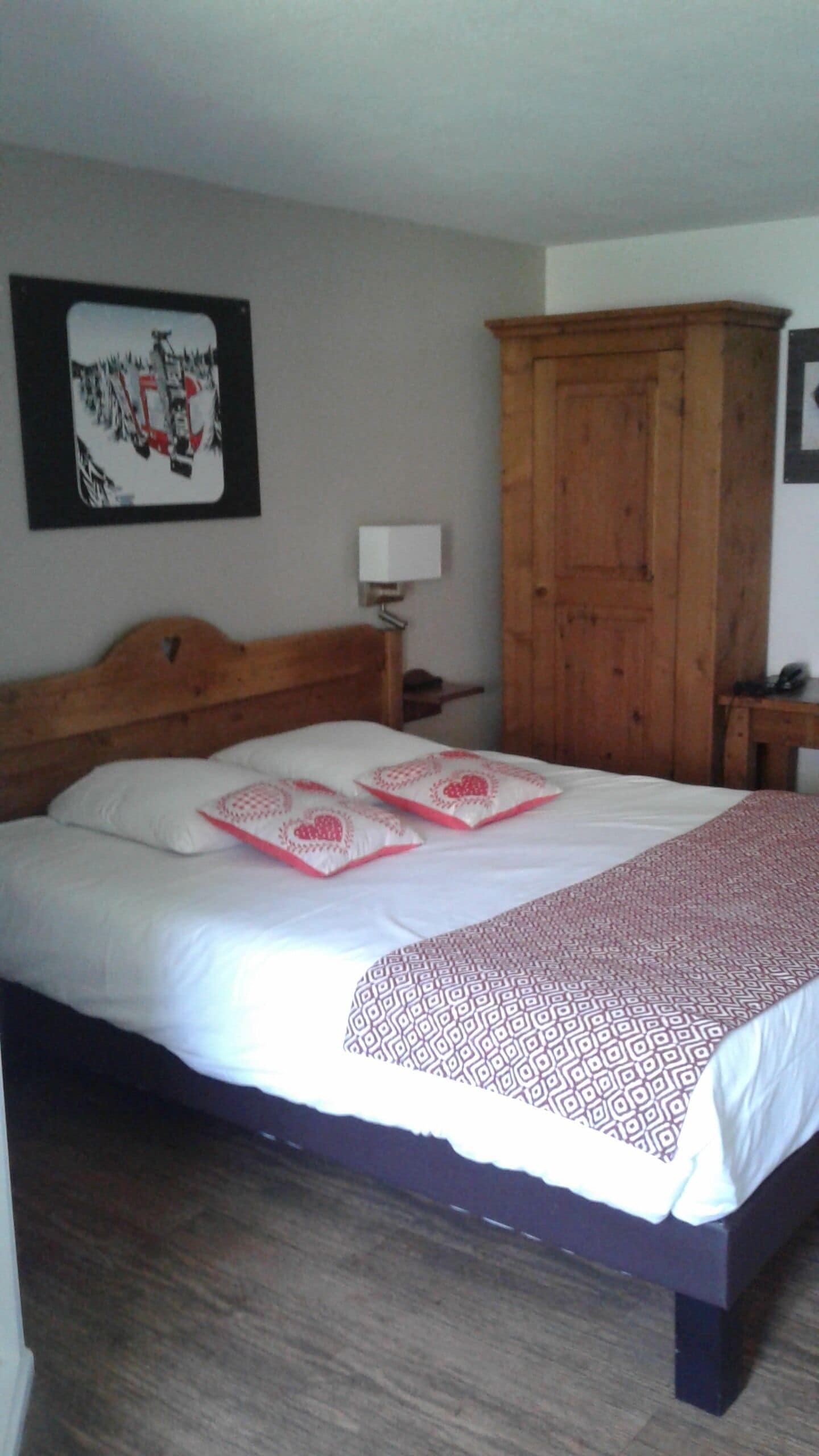 Une chambre à coucher comprenant un lit, une armoire en bois, une table de chevet et une lampe fixée au mur.