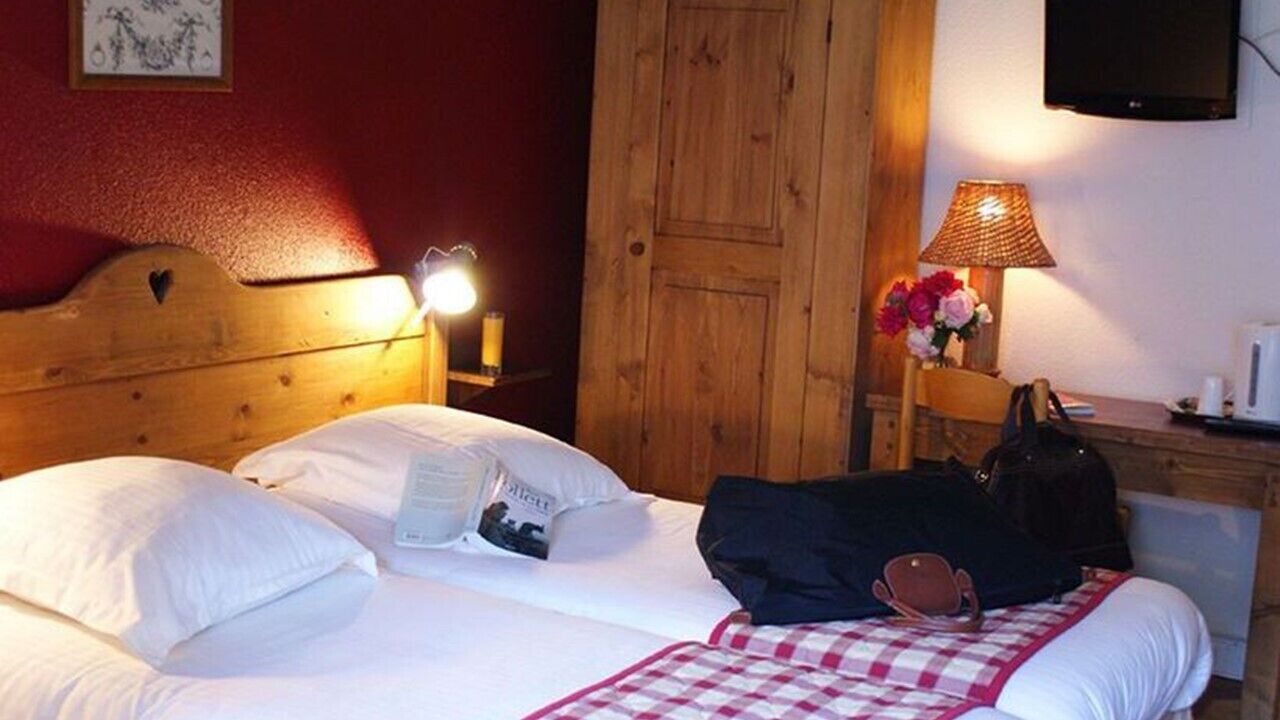 Ein Hotelzimmer mit hölzernem Kopfteil, einer Nachttischlampe, einem Tisch mit Lampe und Blumen sowie einem Koffer auf dem Bett.