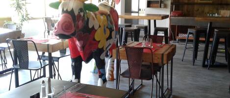 A dining area with tables and chairs, a bull statue, and a kitchen area in the background.