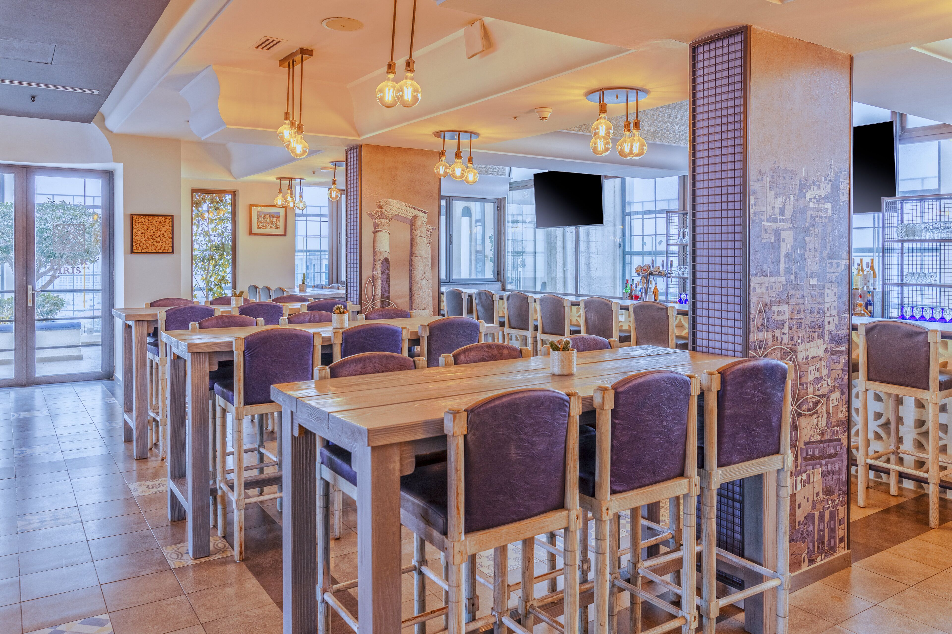 A restaurant with multiple tables and chairs, large windows, and hanging light fixtures.