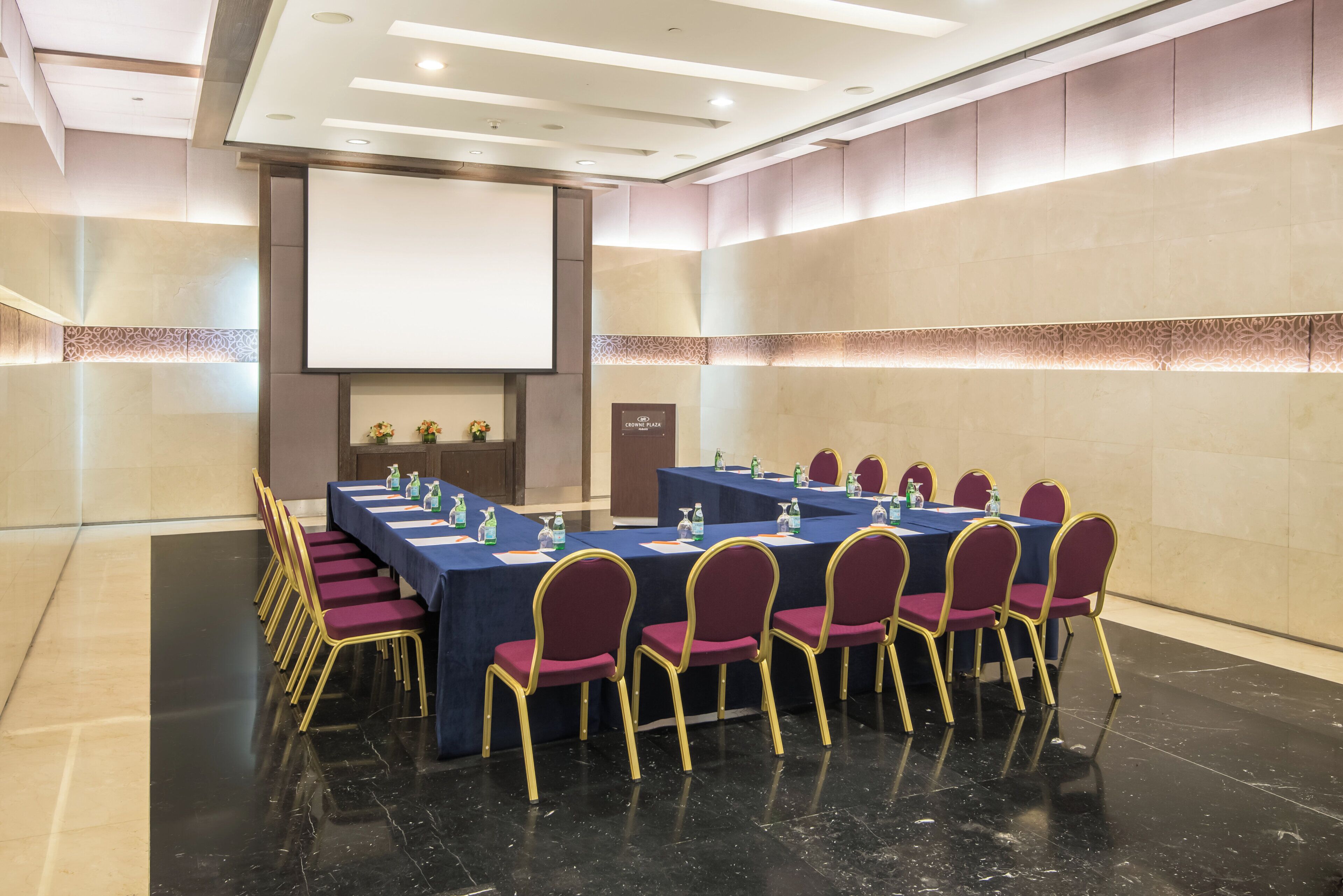 A conference room with a long table, chairs, a projector screen, and a podium.