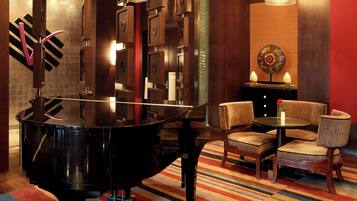 A grand piano in a modern room with a striped carpet, wooden chairs, and a small table with decorative items.