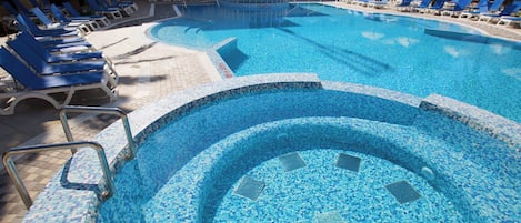 Una piscina con mosaicos azules, rodeada de sillones y sombrillas.