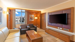 A modern living room with a sofa, two armchairs, a coffee table, a TV, and a city view through large windows. - Crowne Plaza Amman by IHG (Amman)
