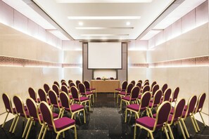 A conference room with rows of chairs facing a podium, a projector screen, and a table with a floral arrangement. - Crowne Plaza Amman by IHG (Amman)
