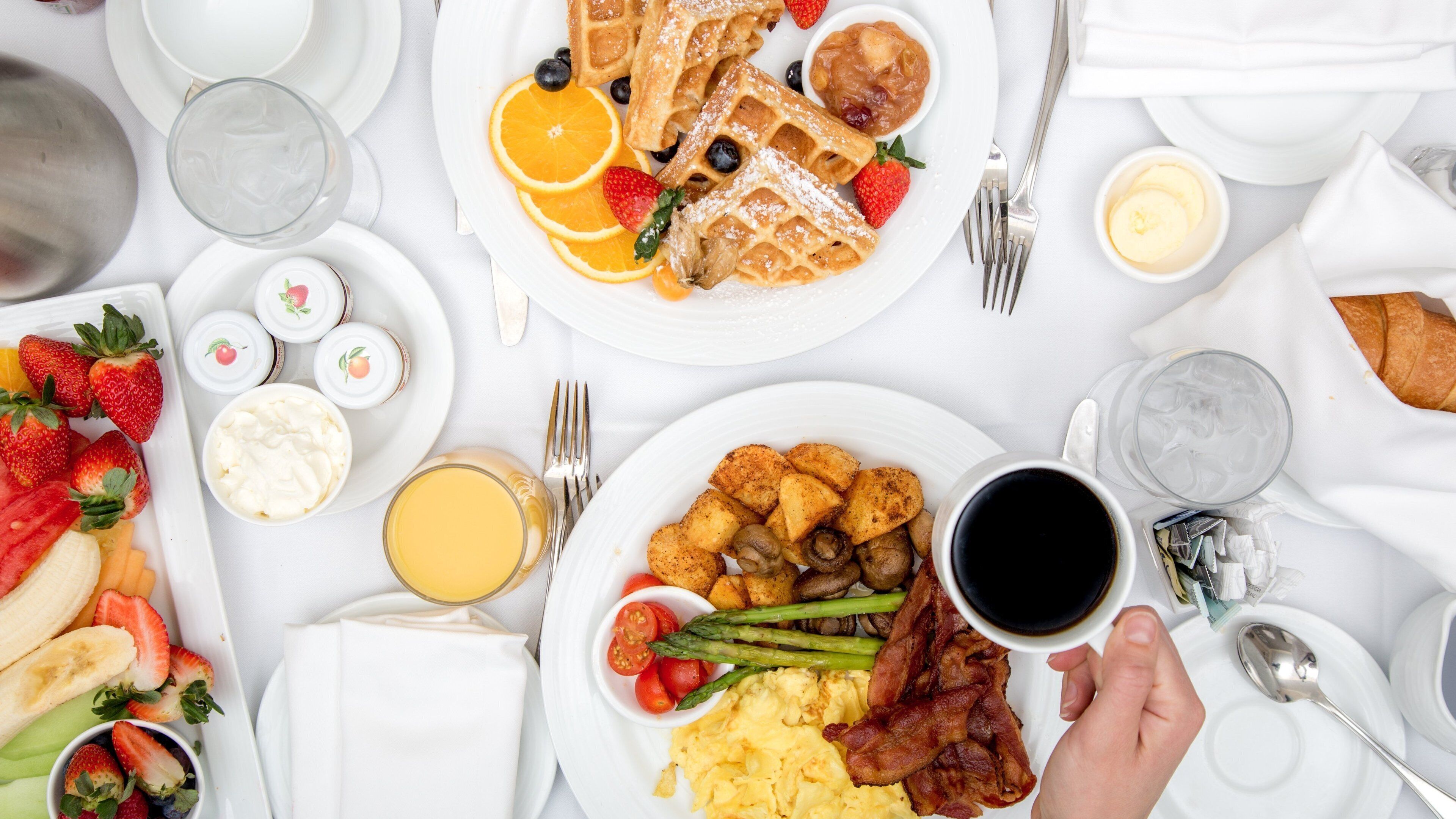 A breakfast table with various dishes including waffles, scrambled eggs, bacon, and fruits.