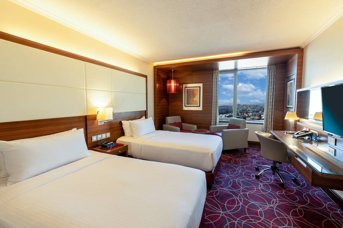 Habitación de hotel con dos camas, un escritorio, una silla y vistas de la ciudad.