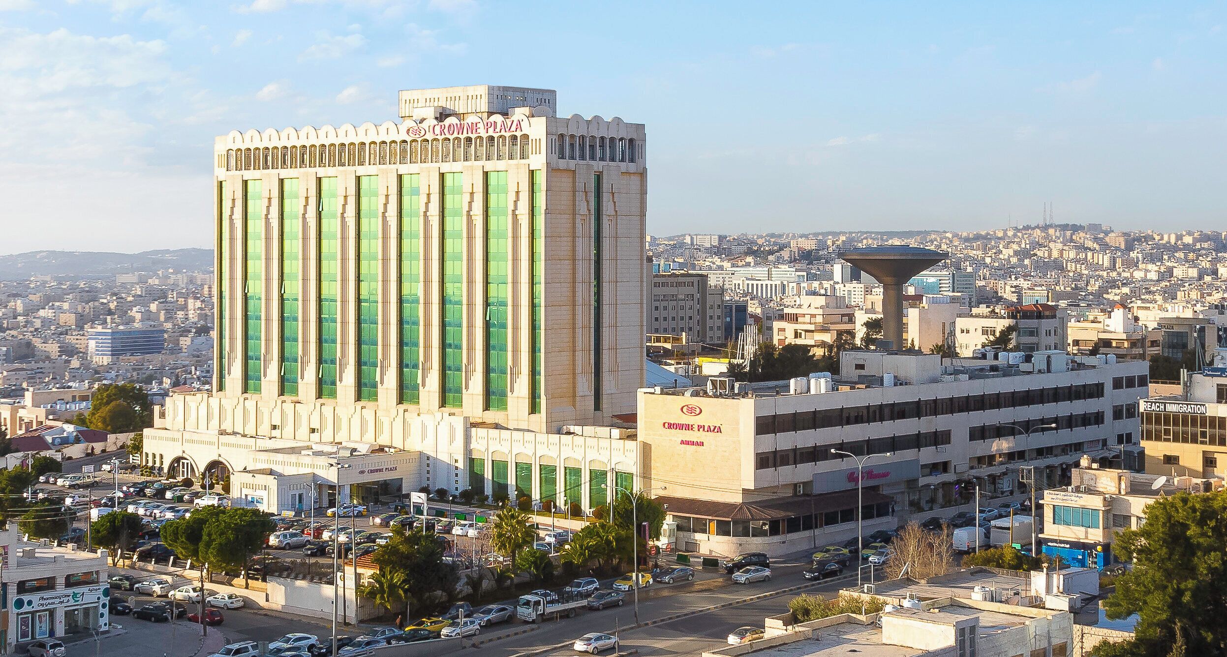 Un grand bâtiment sur lequel on peut lire en grandes lettres « CROWNE PLAZA », et un bâtiment plus petit à côté, portant l’inscription « REACH IMMIGRATION ».