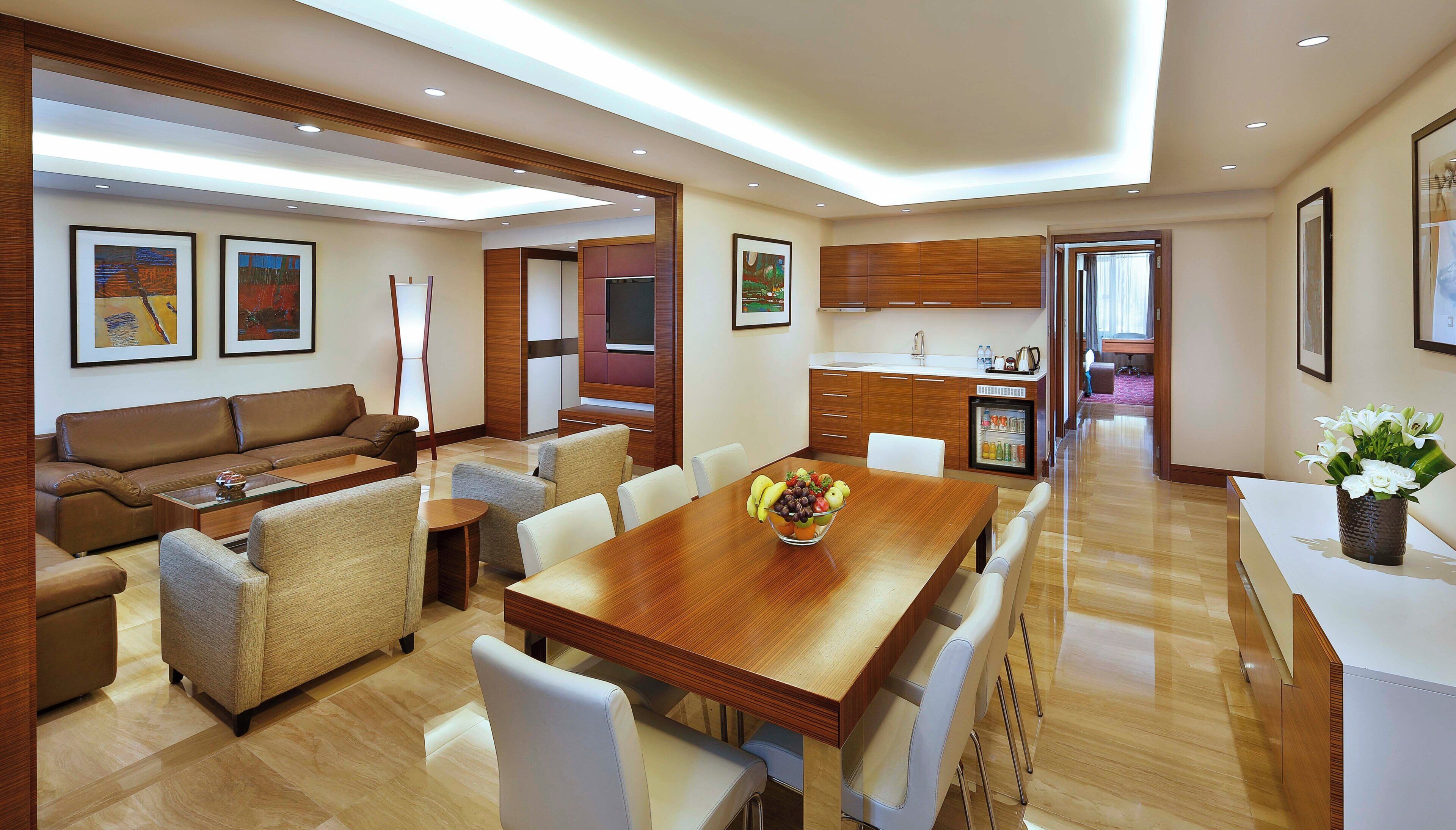 A modern hotel room with a dining area, a sofa, a coffee table, and a fruit bowl.