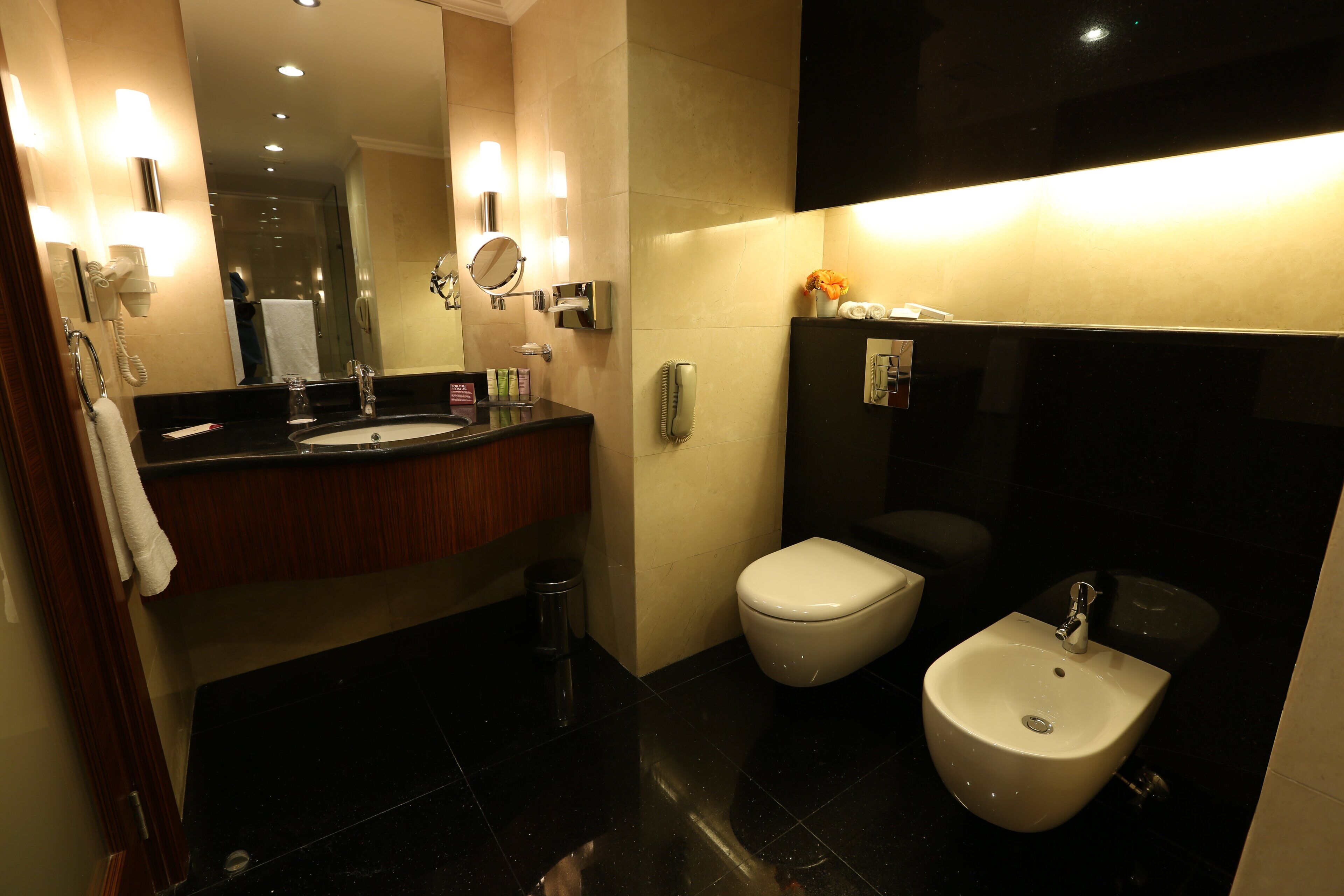 Een moderne badkamer met een wastafel, toilet, bidet en een grote spiegel.