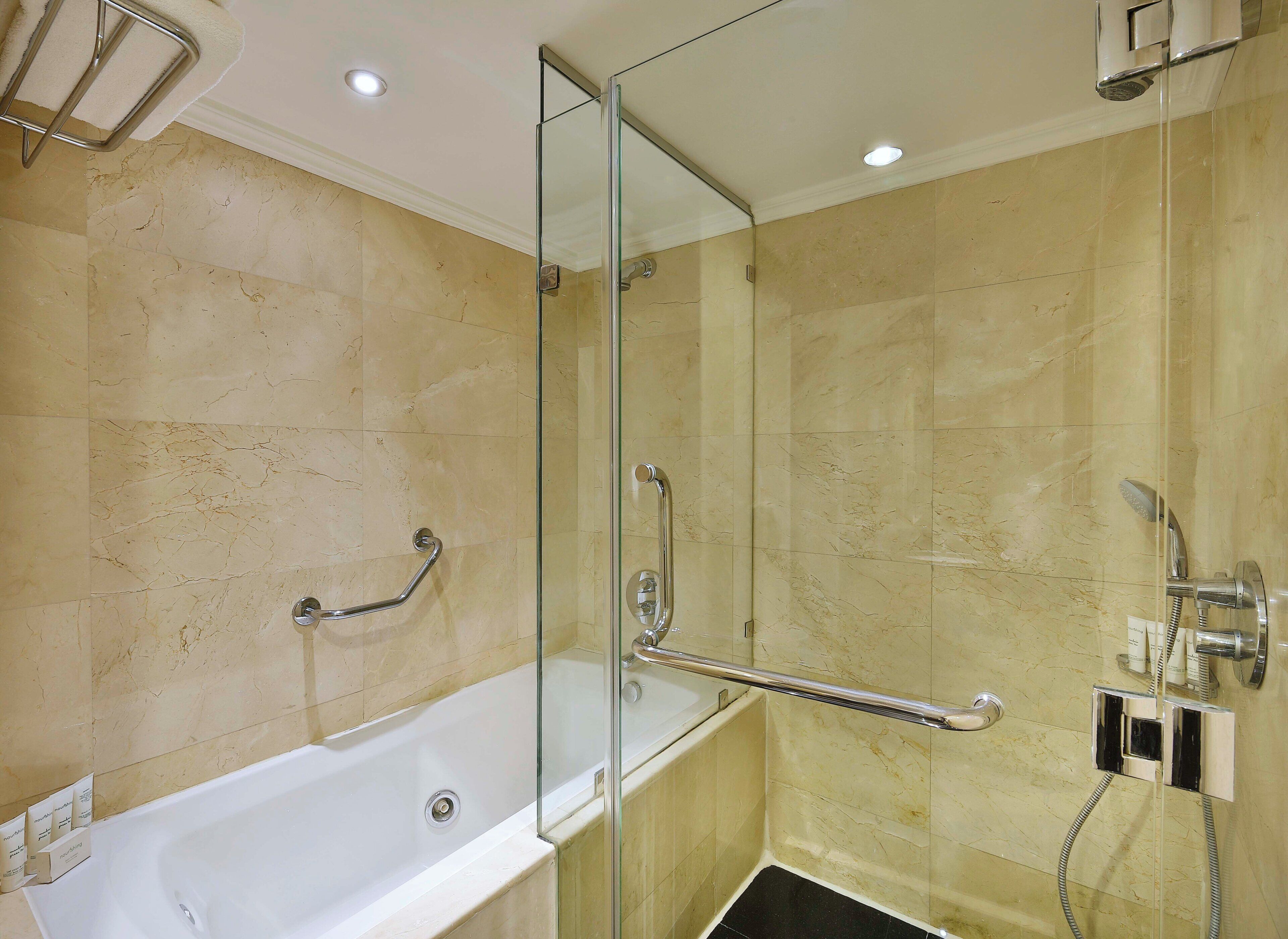 A bathroom with a bathtub, a glass shower enclosure, and a handrail.