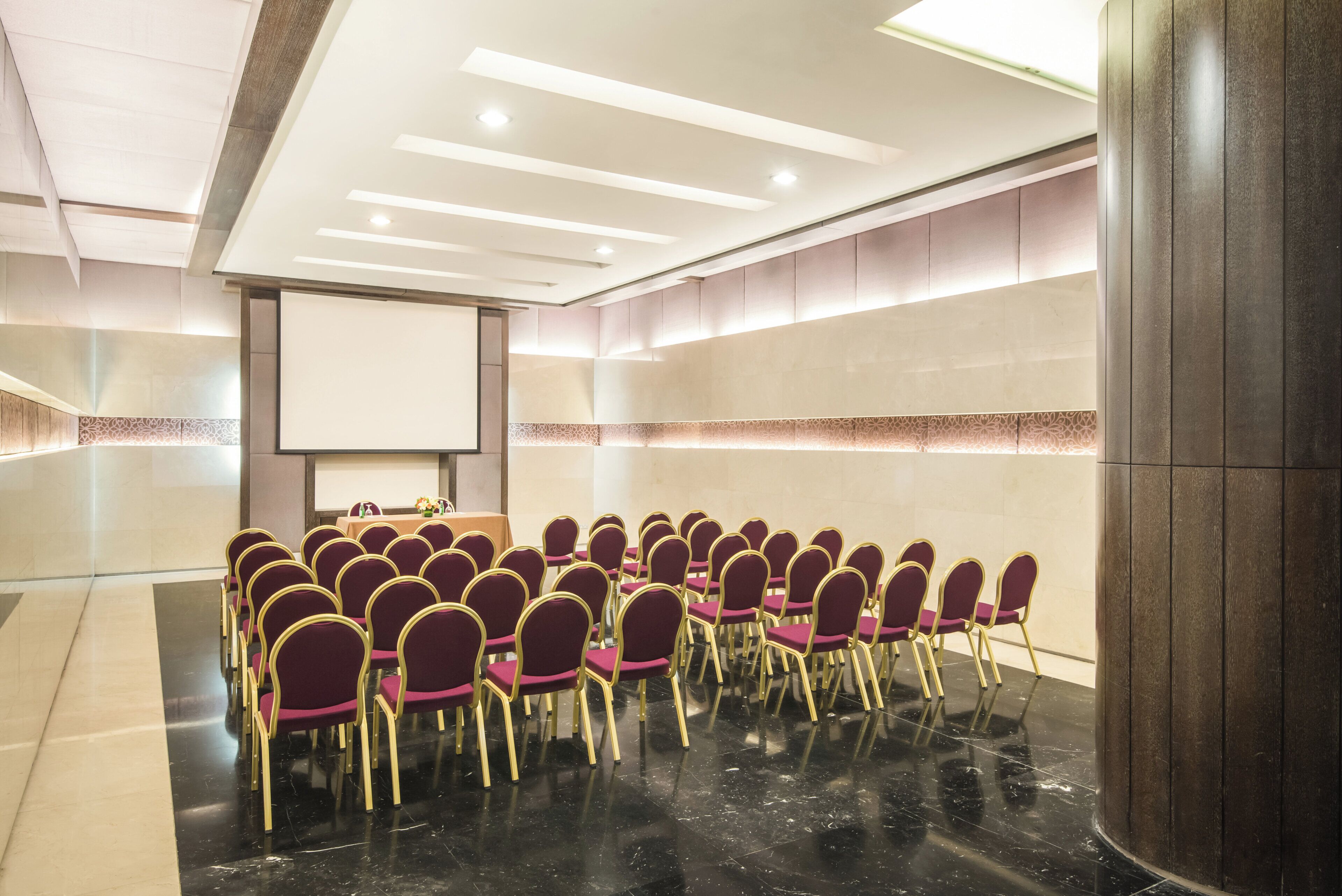 A conference room with rows of chairs, a projector screen, and a presentation area.