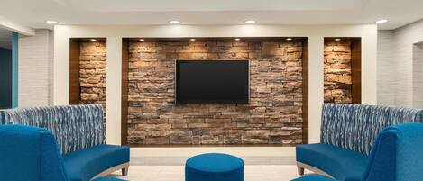 A modern lounge area with a stone wall, a flat-screen TV, and blue upholstered seating.