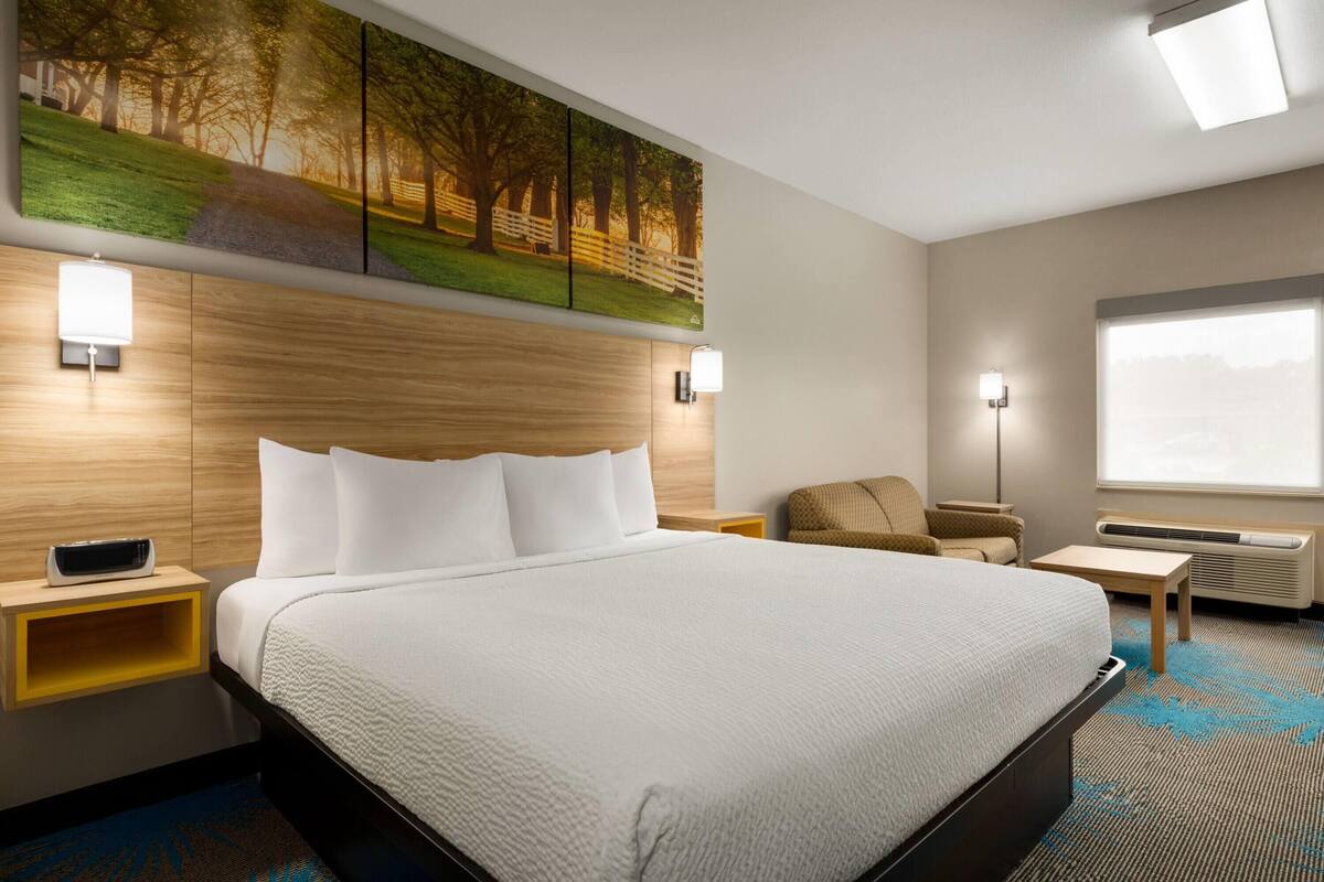 Un cuarto de hotel con una cama grande, un cabecero de madera, un cuadro sobre la cama, un escritorio, una silla y una ventana con vistas.
