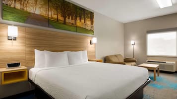 A hotel room with a large bed, a wooden headboard, a painting above the bed, a desk, a chair, and a window with a view.