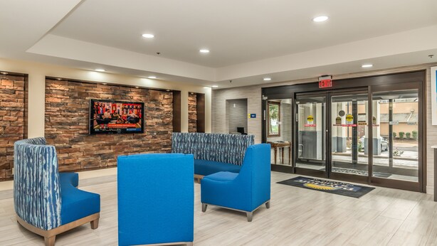 A lobby with blue seating, a stone wall, a television, and an exit door. - Days Inn & Suites by Wyndham Prattville-Montgomery (Prattville)