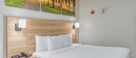 A hotel room with a wooden headboard, white bedding, a bedside table with a phone and charger, and a yellow storage box.