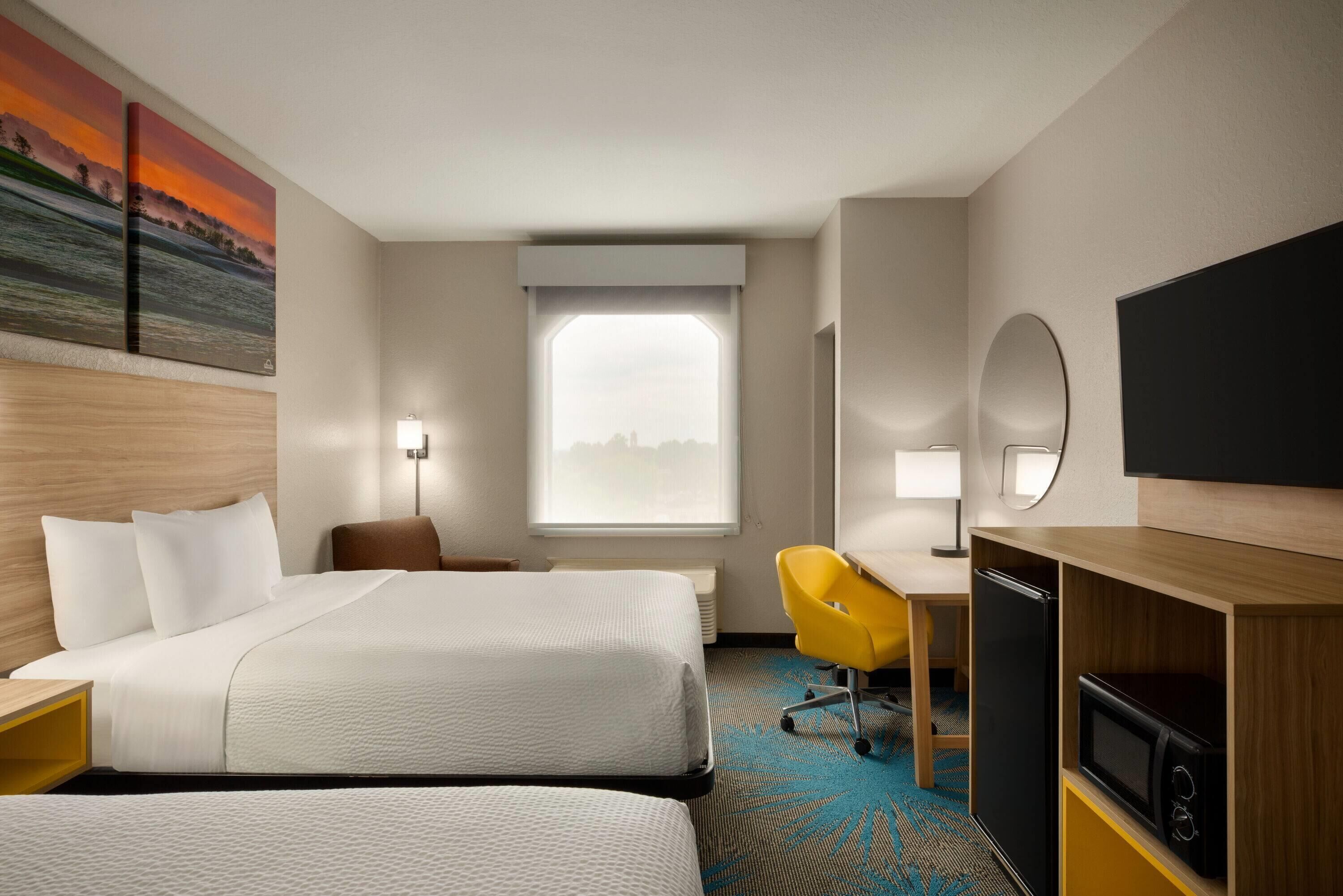 Quarto de hotel com duas camas, uma escrivaninha, uma cadeira, uma televisão e janela com vista.
