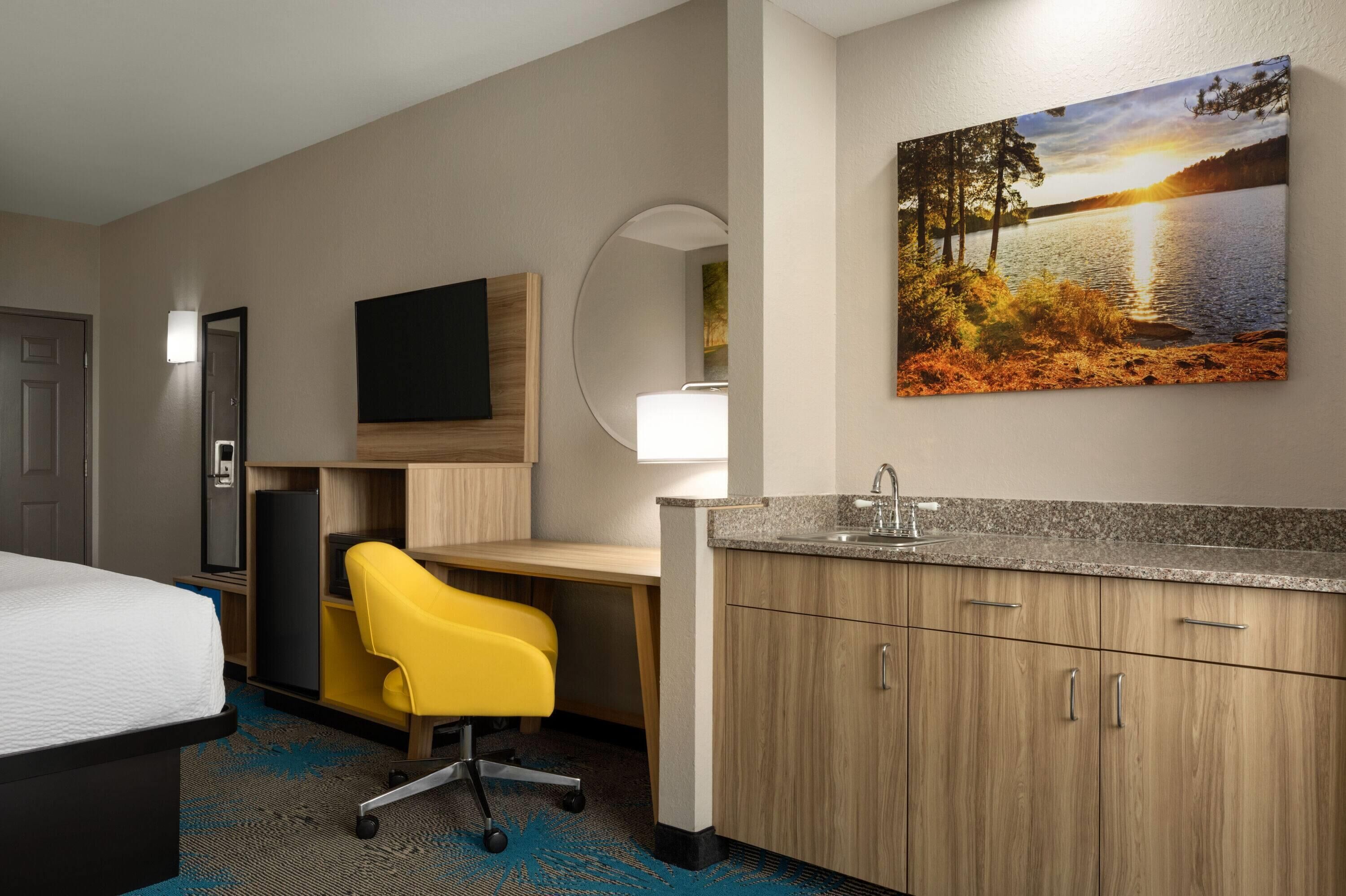 Une chambre d’hôtel avec un lit, un bureau, une chaise, une télévision, un tableau et un lavabo.