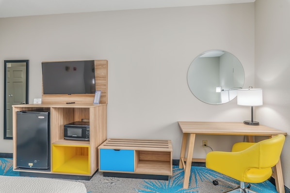 Habitación de hotel compacta con cama, un escritorio de madera con una silla amarilla, un televisor de pantalla plana, microondas y un refrigerador pequeño.