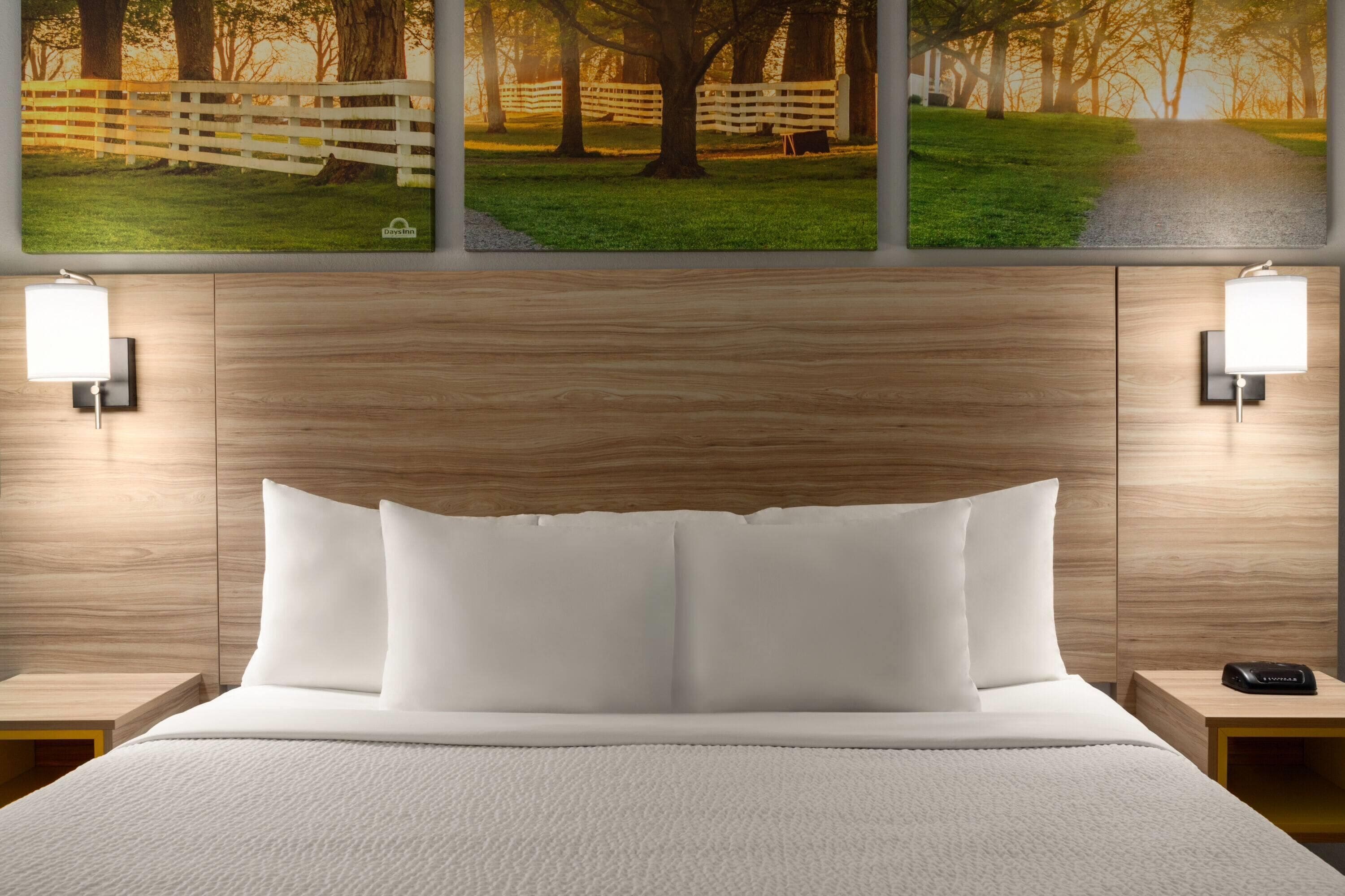 Een opgemaakt bed met witte lakens, een houten hoofdbord en twee nachtkastjes met lampen.