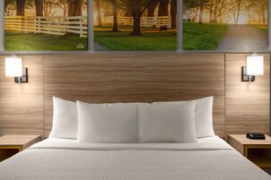 Uma cama bem arrumada com roupa de cama branca, cabeceira de madeira e duas mesas de cabeceira com abajures.