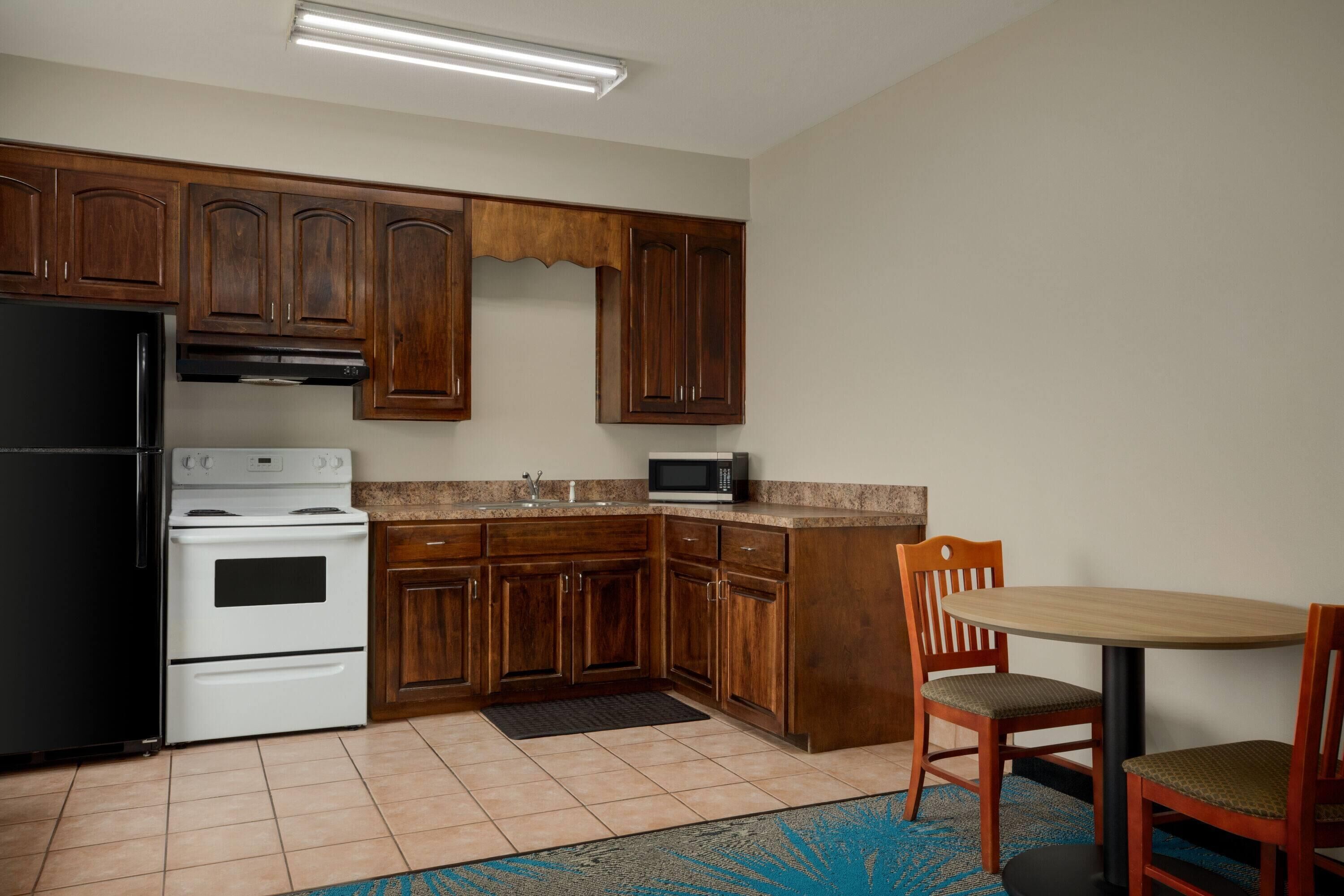 Una cocina con armarios de madera, una estufa blanca, un microondas y una zona de comedor con dos sillas.