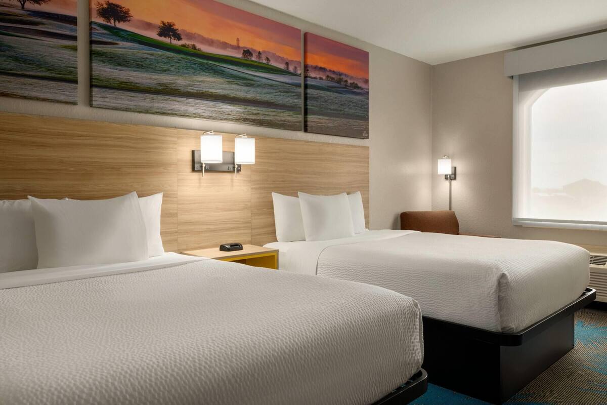 Habitación de hotel con dos camas, cabecera de madera, luces fijadas a la pared y un ventanal grande.