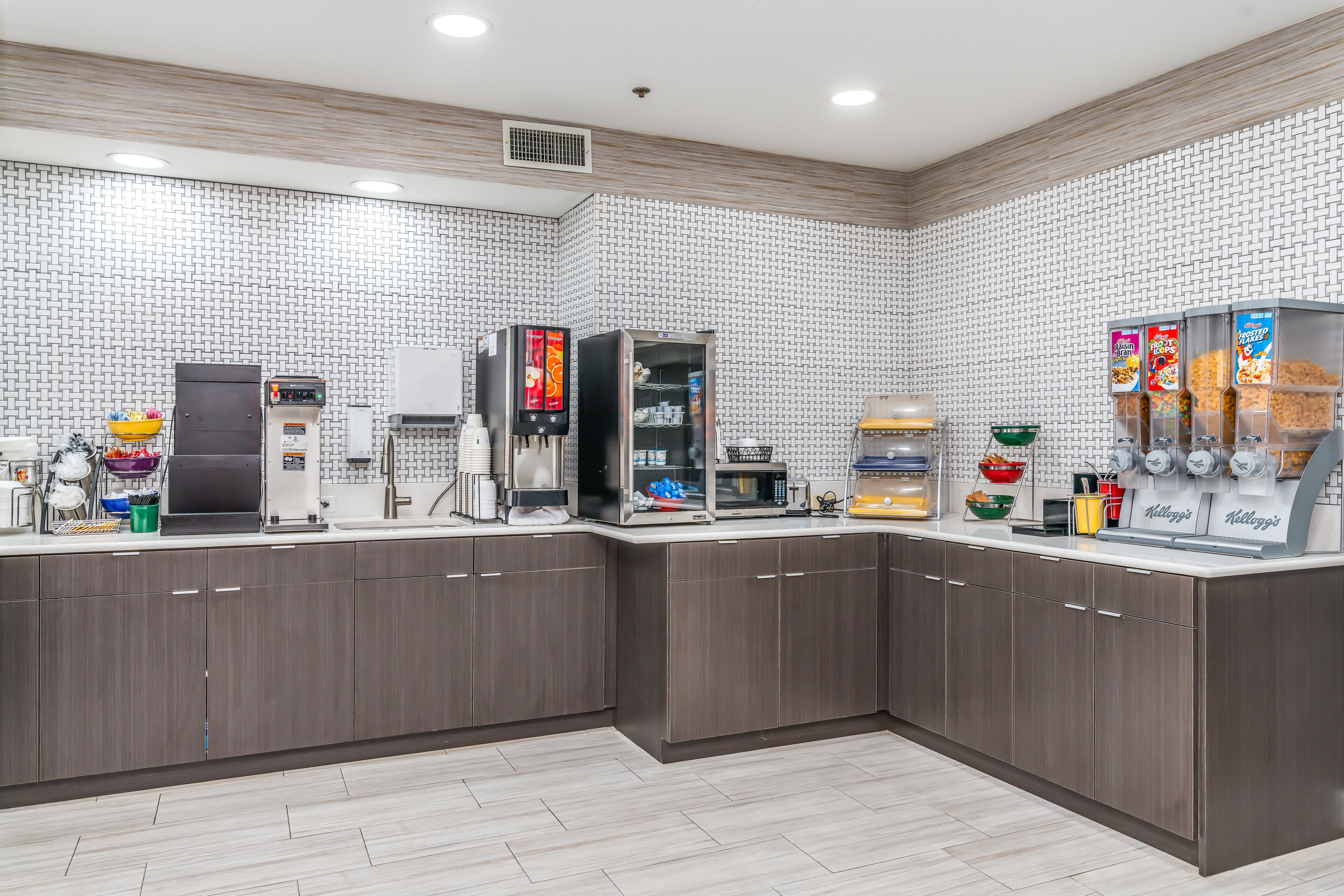 A modern kitchen with a microwave, coffee machine, and beverage dispensers.