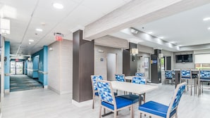 A modern dining area with blue and wooden chairs, a white table, and a TV screen. - Days Inn & Suites by Wyndham Prattville-Montgomery (Prattville)