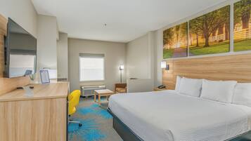 A hotel room with a large bed, a desk with a computer, a chair, and a window.