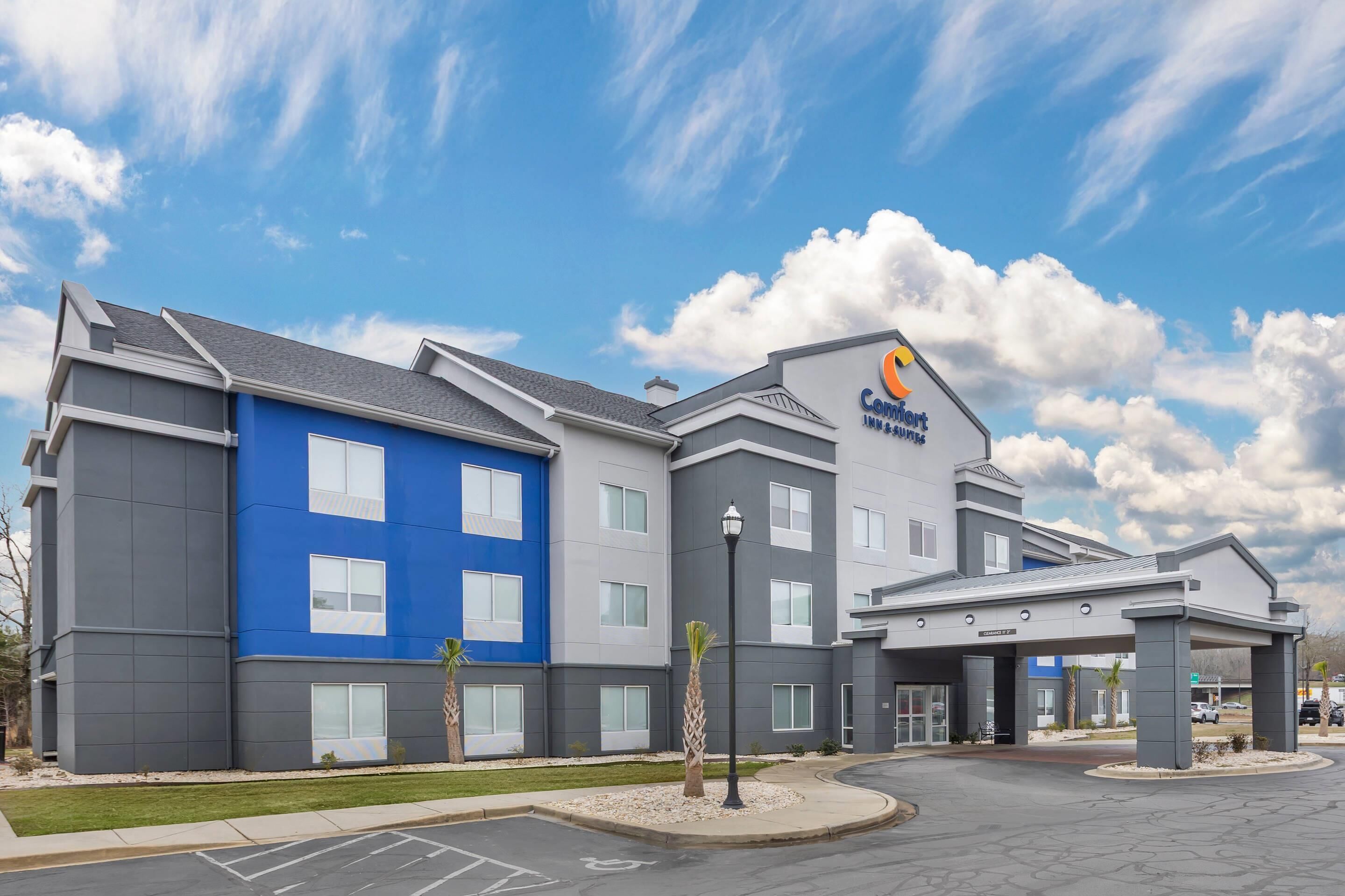 Een Comfort Inn hotel met een blauw-grijze gevel, veel ramen en een parkeerplaats.