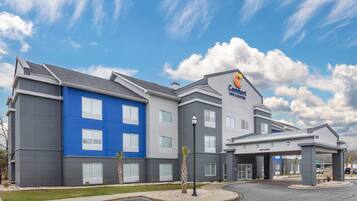 Een Comfort Inn hotel met een blauw-grijze gevel, veel ramen en een parkeerplaats.