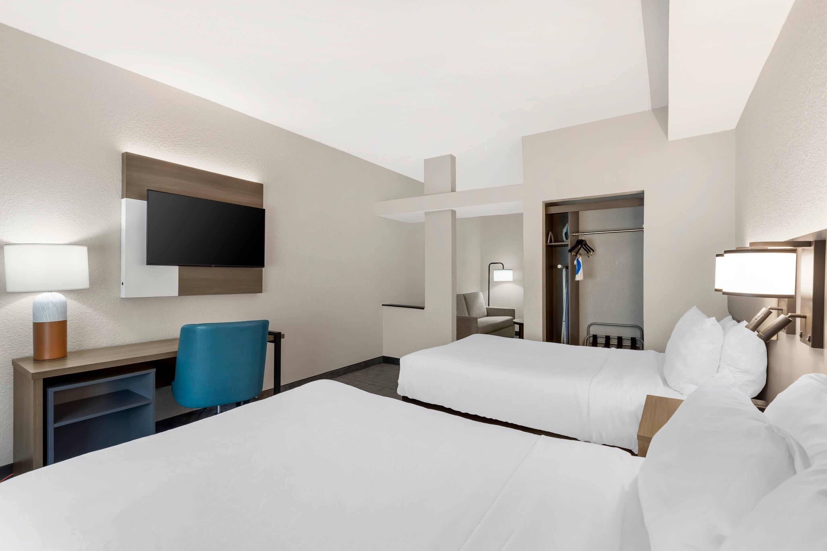 Une chambre d’hôtel avec deux lits, un bureau, une chaise, une télévision et une armoire.
