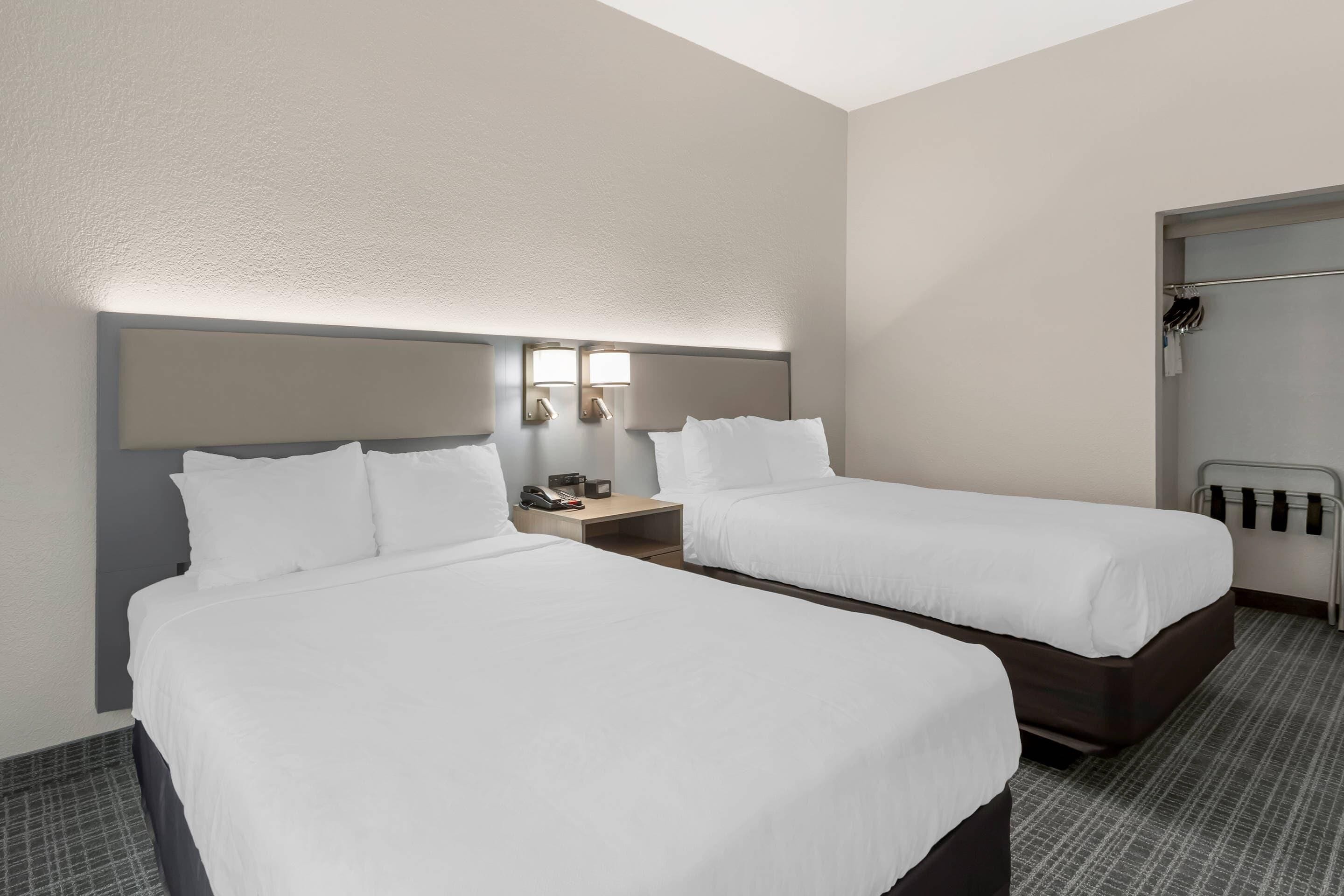 Ein Hotelzimmer mit zwei Betten, einem Nachttisch mit Telefon und Lampe sowie einem Kleiderständer.