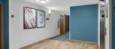 Un couloir avec un plancher en bois, des murs bleus et deux tableaux encadrés accrochés au mur.